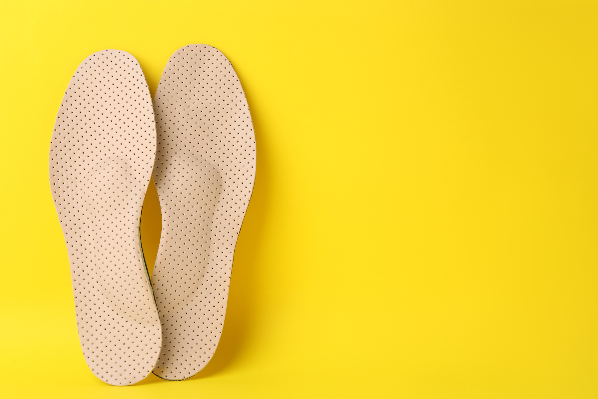 Beige Custom Orthotics on yellow background, flat lay. Space for text