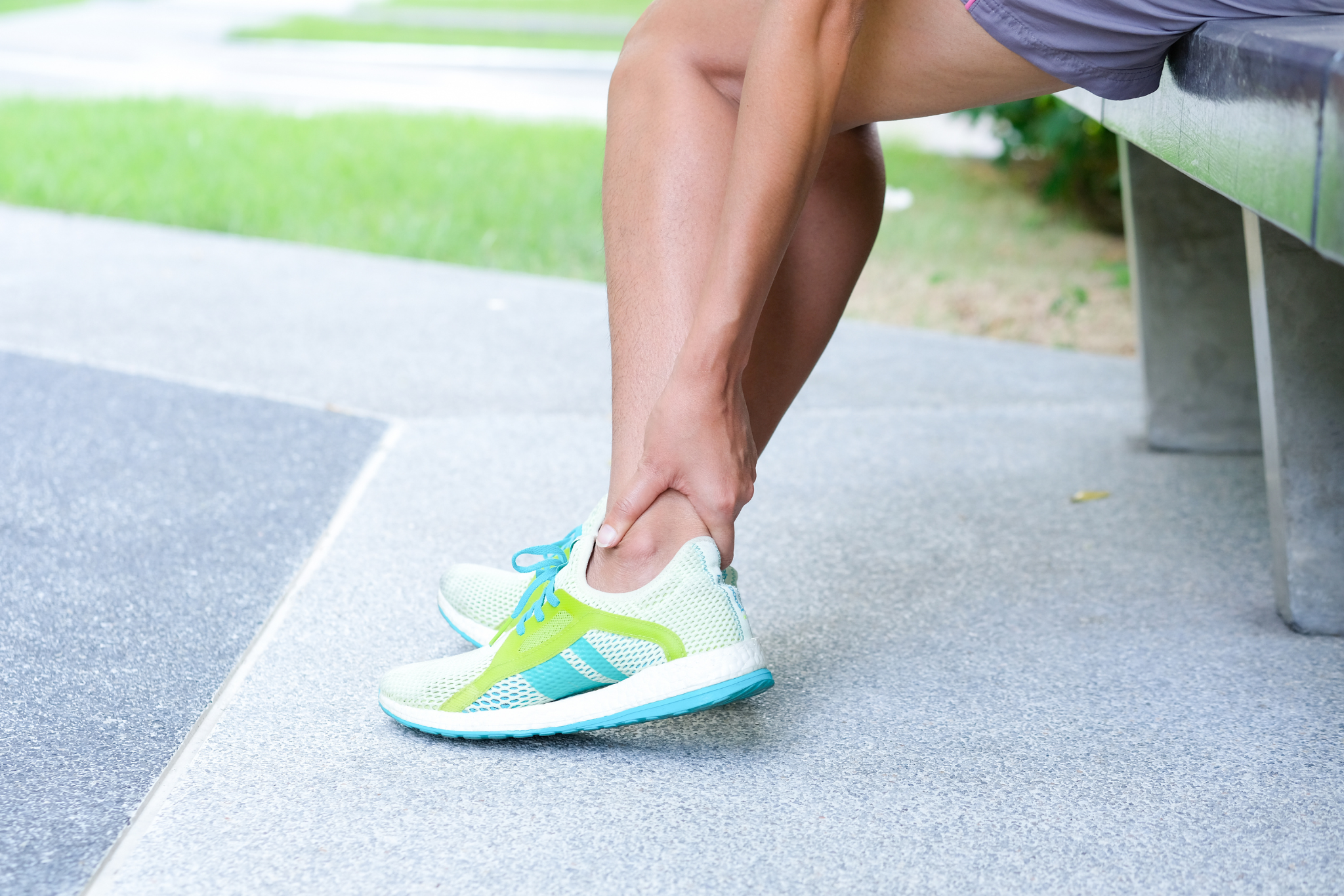 Foot Pain Leg of woman which runner athletic by running shoes sitting on grass in the park holding he feet and stretch the muscles in morning sunlight .Health care concept